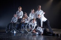 8 Tänzer/innen mit und ohne Behinderung formieren sich auf der Bühne als Gruppe.